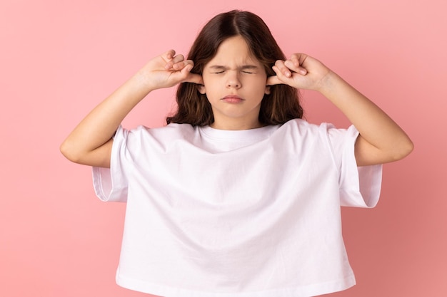 Geïrriteerd meisje in wit T-shirt dat oren bedekt en ogen dicht houdt zenuwinzinking