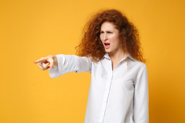 Geïrriteerde jonge roodharige vrouw meisje in casual wit overhemd poseren geïsoleerd op geel oranje muur