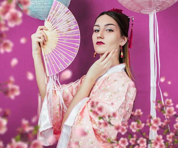 Geisha in pink kimono and with a fan close-up on a purple wall and with blurred sakura flowers