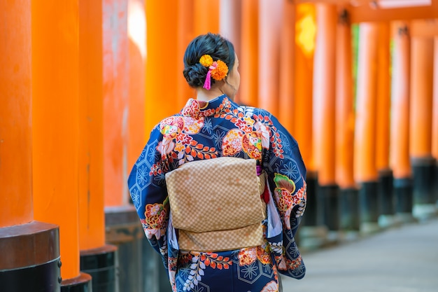 京都の伏見稲荷大社で赤い木製の鳥居の中で日本の着物を着ている芸者の女の子、