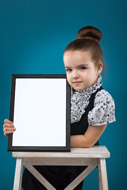 Geïsoleerd op blauw, aantrekkelijk Kaukasisch kind houdt grote lege poster