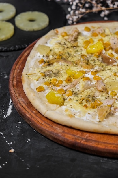 Geïsoleerd Pizza met kip en ananas op een houten bord en op een donkere ondergrond