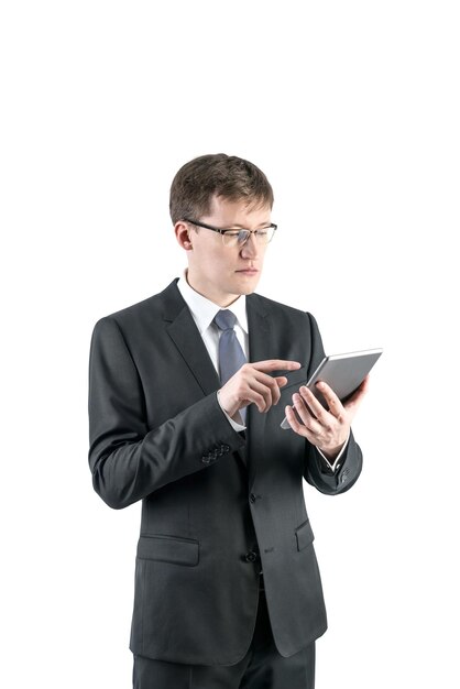 Geïsoleerd portret van een knappe zakenman met licht haar die een donker pak draagt met een stropdas en een bril en met een digitale tablet werkt.