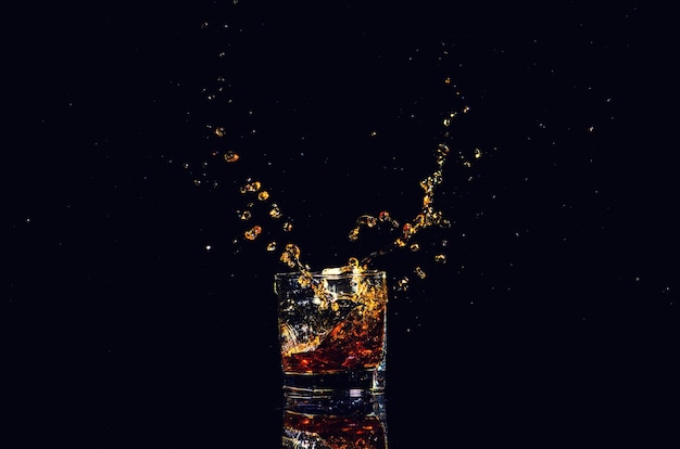 Geïsoleerd schot van whisky met plons op zwarte cognac als achtergrond in een glas