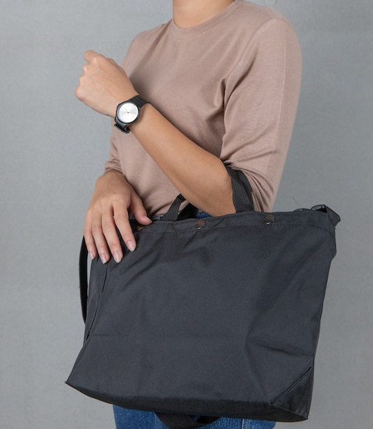 Geïsoleerde close-up studio shot van grote zwarte casual trendy mode stof handtas bagage opknoping op vrouw arm draagt shirt met lange mouwen en jeans met polshorloge staande voor witte achtergrond.