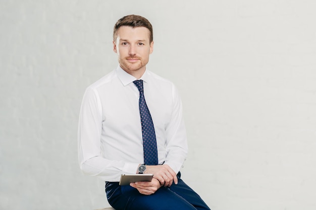 Geïsoleerde shot van succesvolle mannelijke manager draagt elegante witte overhemd zwarte broek en stropdas maakt gebruik van moderne tabletcomputer voor werk en entertainment geïsoleerd op witte achtergrond Bedrijfsconcept