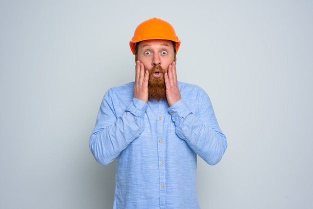 Geïsoleerde verbaasde architect met baard en oranje helm