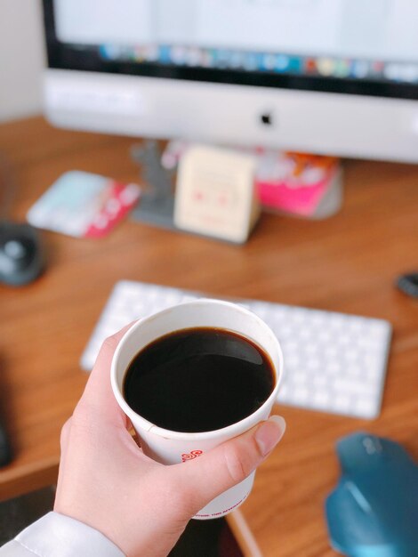 Foto gekapte afbeelding van een hand die een koffiekop op tafel houdt