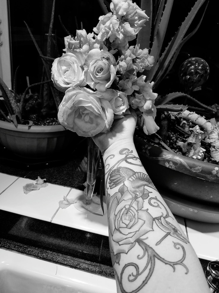 Foto gekapte afbeelding van een hand met een tatoeage die rozen vasthoudt bij potplanten