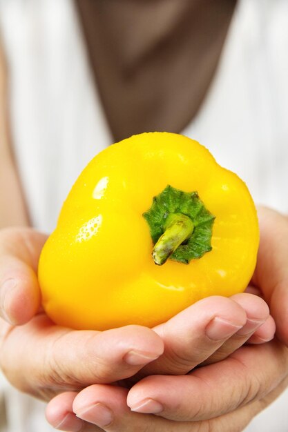 Gekapte afbeelding van een persoon die gele peper vasthoudt