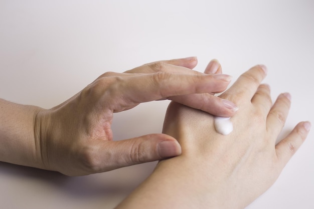 Gekapte afbeelding van een vrouw die crème op haar hand aanbrengt tegen een witte achtergrond