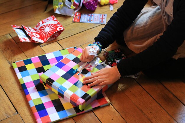 Foto gekapte afbeelding van een vrouw die een lint bindt op een geschenkdoos op een hardhouten vloer