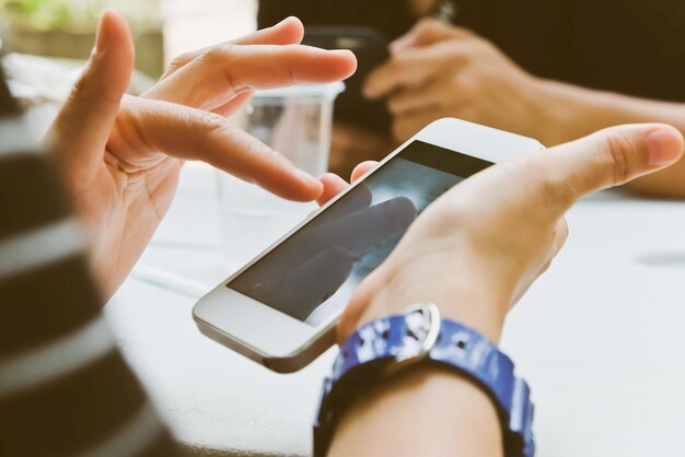 Foto gekapte afbeelding van een vrouw die een mobiele telefoon gebruikt met een vriend op de achtergrond