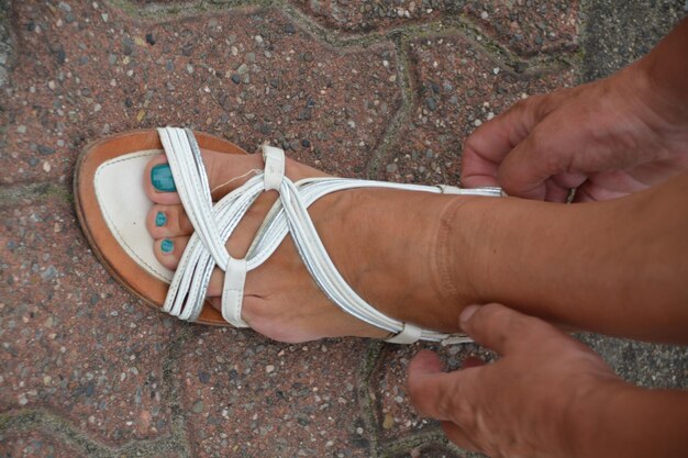 Foto gekapte afbeelding van een vrouw die een sandal aanpast op een voetpad