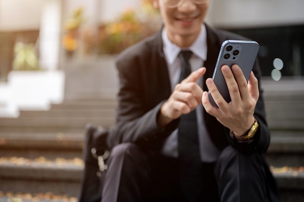 Gekapte afbeelding van een zakenman die zijn smartphone gebruikt terwijl hij op een trap zit