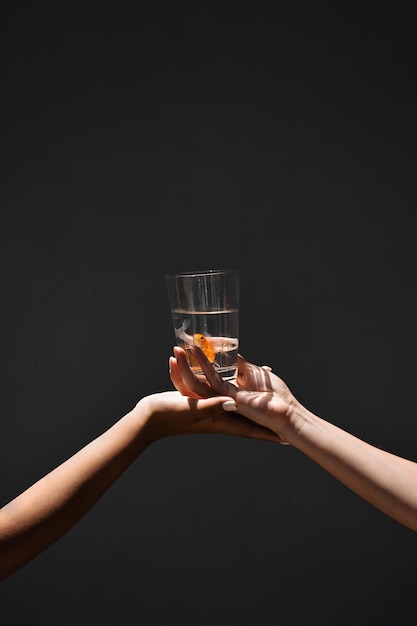 Gekapte afbeelding van handen die vissen in glas vasthouden tegen een zwarte achtergrond