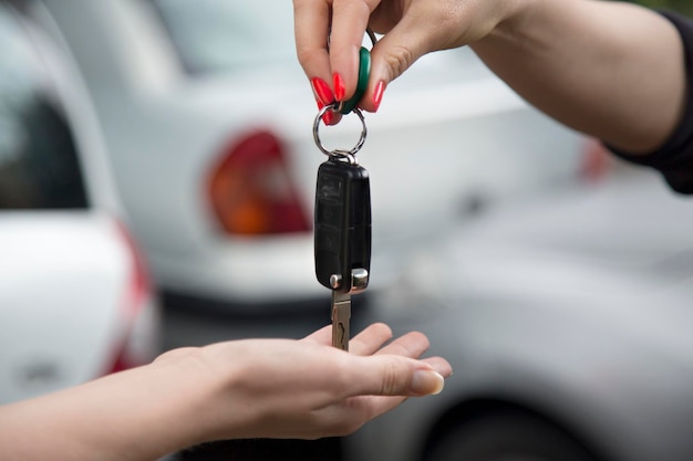 Foto gekapte hand die de autosleutel aan een vrouw geeft.