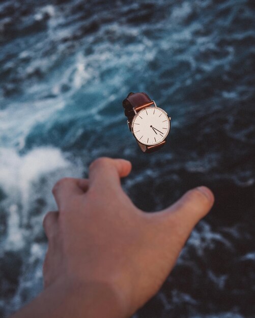 Foto gekapte hand die een horloge over zee bereikt