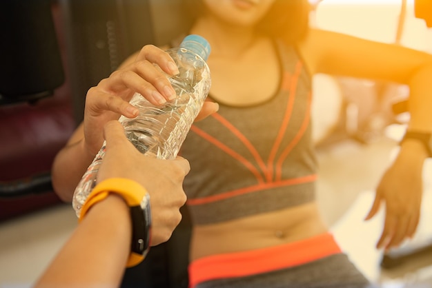 Foto gekapte hand die een waterfles geeft aan een vrouw in de sportschool.