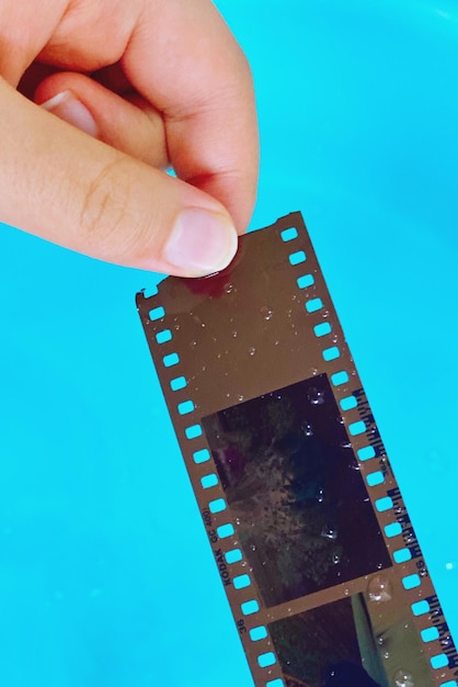 Foto gekapte hand die filmrol vasthoudt tegen blauwe achtergrond