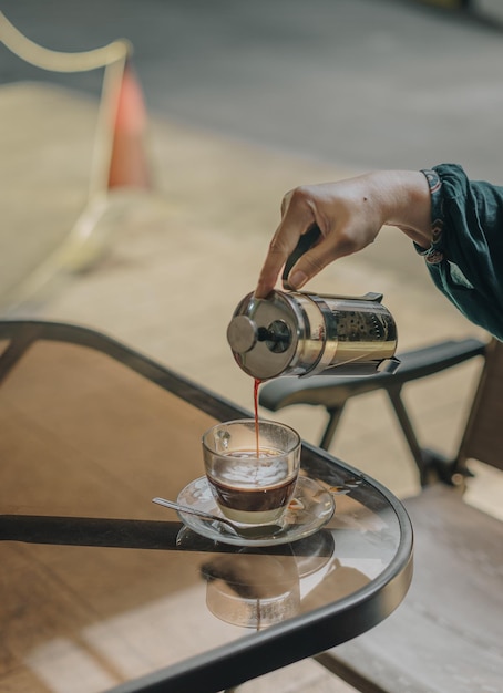 Gekapte hand die koffie in een kopje bij de tafel schenkt