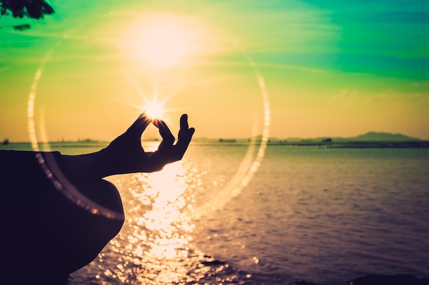 Foto gekapte hand doet yoga bij het meer bij zonsopgang