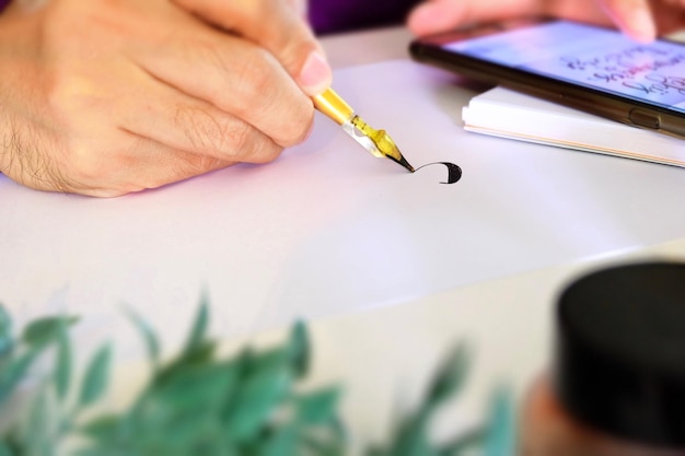 Gekapte hand met behulp van een mobiele telefoon tijdens het oefenen van kalligrafie op papier