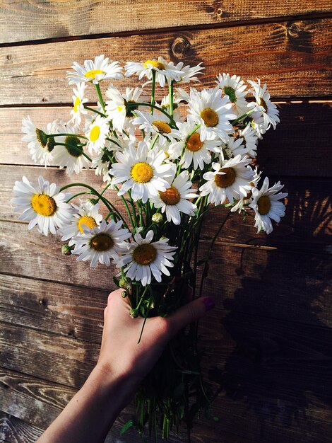 Gekapte hand met een boeket bloemen tegen een houten muur