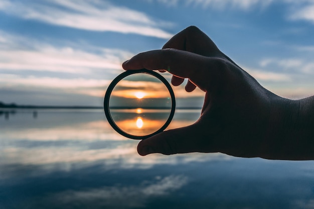 Foto gekapte hand met glas aan de oever van het meer tegen de lucht