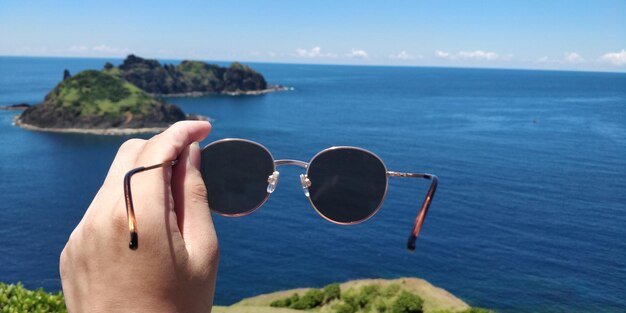 Foto gekapte hand met zonnebril tegen de zee.