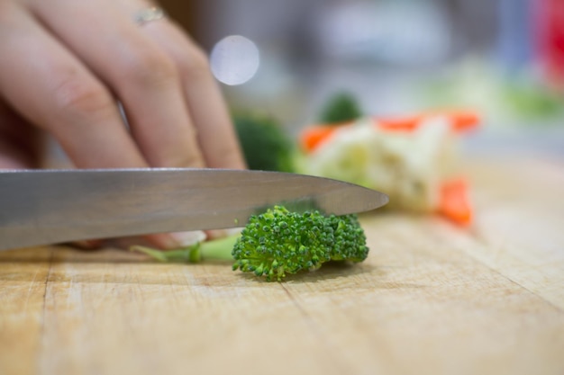 Gekapte hand op vrouw die broccolini snijdt in de keuken.