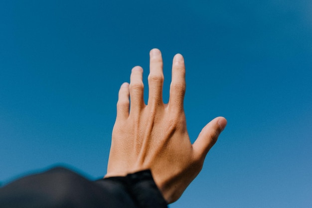 Gekapte hand van een man die naar de heldere blauwe hemel reikte.
