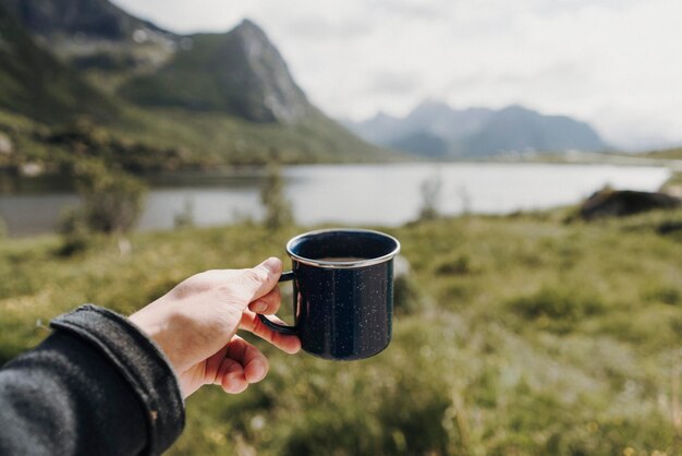 Foto gekapte hand van een persoon die een koffiekop tegen het meer houdt