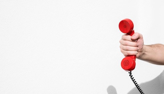 Gekapte hand van een persoon die een rode telefoon tegen de muur houdt