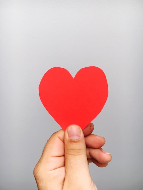 Gekapte hand van een persoon die een rood hartvormig lijmbriefje vasthoudt op een grijze achtergrond.