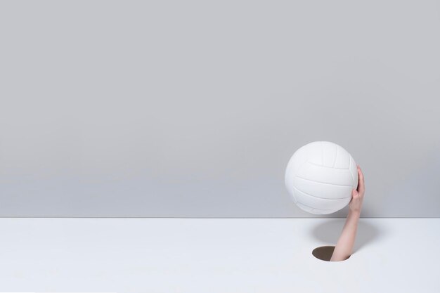 Foto gekapte hand van een persoon die een volleybal vasthoudt op een grijze achtergrond