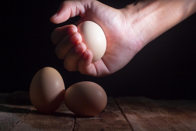 Gekapte hand van een vrouw die een ei vasthoudt boven een houten tafel