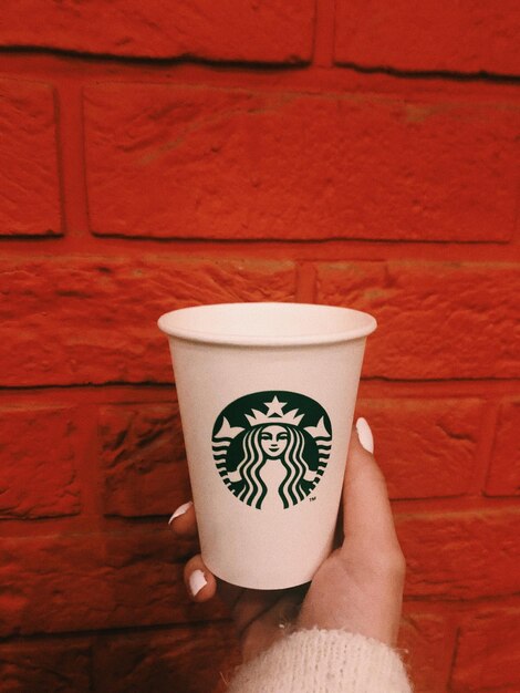 Foto gekapte hand van een vrouw die een koffiekop tegen een bakstenen muur houdt