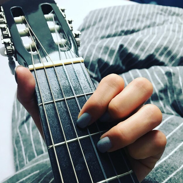 Foto gekapte hand van een vrouw die gitaar speelt op bed.