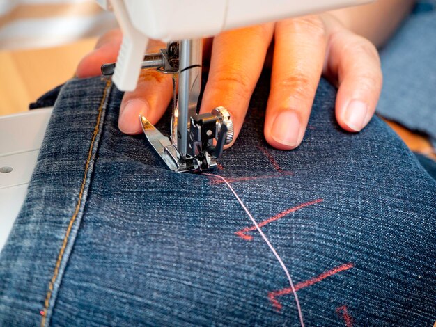 Gekapte hand van een vrouw die spijkerbroek naait