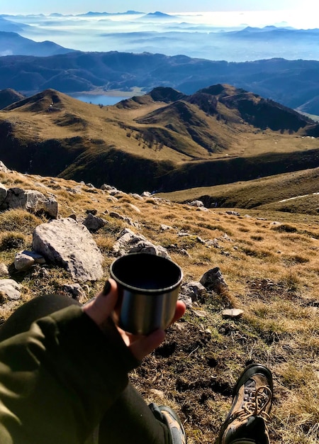 Foto gekapte hand van een vrouw met een koffiekop tegen het landschap