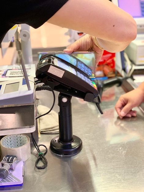 Foto gekapte hand van een vrouw met een smartphone bij een creditcardlezer terwijl ze in een winkel betaalt