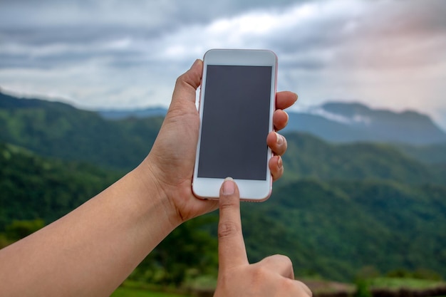 Gekapte hand van een vrouw met een smartphone tegen een bergketen