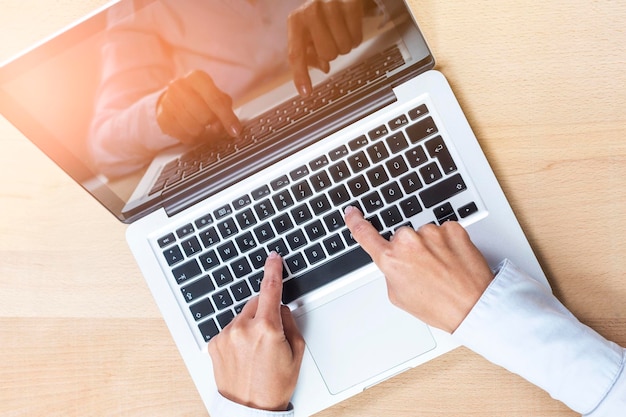 Gekapte handen die aan een laptop werken.