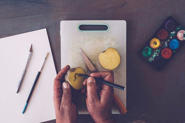 Foto gekapte handen maken kerstboom op gehalveerde aardappel met viltpen aan tafel