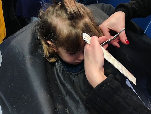 Foto gekapte handen van een kapper die het haar van een meisje snijdt.