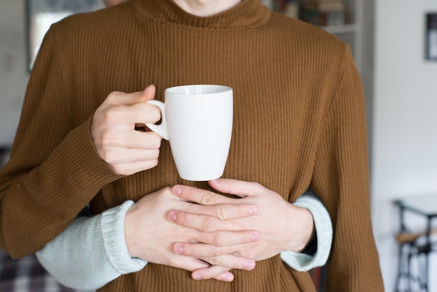 Foto gekapte handen van een man die zijn vriendje omarmt met een beker in zijn hand.