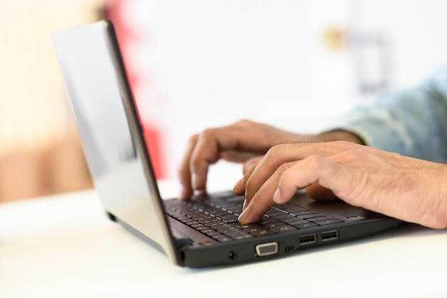 Gekapte handen van een man met een laptop op tafel.