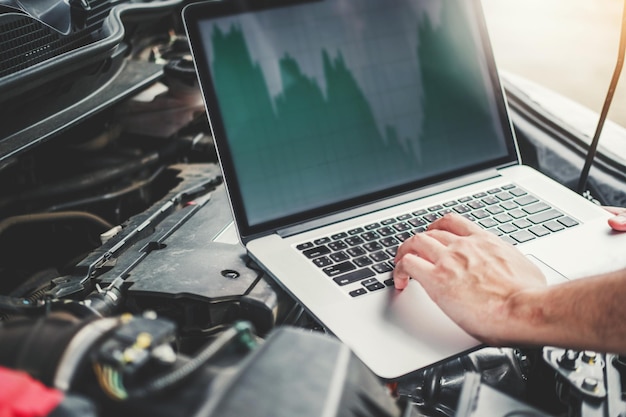 Foto gekapte handen van een monteur met een laptop op de motor van een auto.