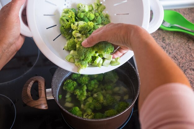 Gekapte handen van een persoon die broccoli bereidt